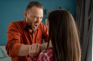 Aile içi şiddet, taciz konsepti. Güçlü adam korkmuş kadını oturma odasında boğuyor. Yakın plan..