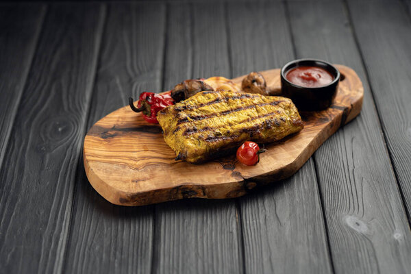 Grilled chicken meat served with vegetables and tomato sauce on a wooden board, top view, flat lay. Food and summer concept