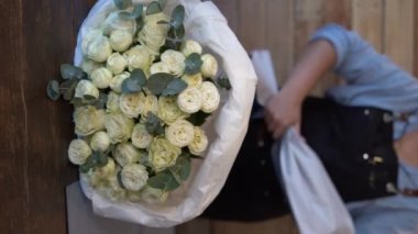 Çiçek teslimat konsepti. Çiçekçi kadın büyük bir buket beyaz gül yapıyor. Masterclass ve çiçekçi kursları. Dikey video