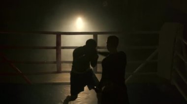 Boks eldivenli genç adam antrenörüyle boks yapıyor. Yumruklardan kaçmak ve boks ringinde pratik yapmak. Boşluğu kopyala