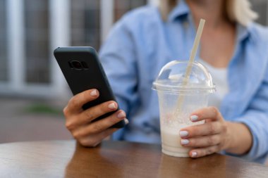 Cafe City yaşam tarzı. Akıllı telefon kullanan, sütlü kokteyl içen akıllı telefon uygulamasından mesaj atan bir kadın. Yakın plan.