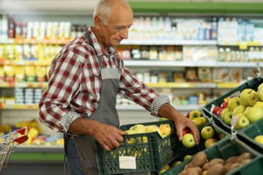 Markette kıdemli bir adam, süpermarkette. Sebze reyonundaki raflara yiyecek koymak. Boşluğu kopyala