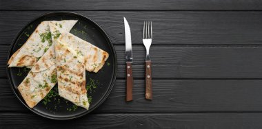 Lavaşlı suluguni peyniri, siyah ahşap arka planda, çatal bıçaklı otlarla servis edilir. Pankart. Boşluğu kopyala