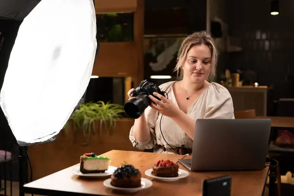 Female food photographer with laptop computer and camera photographing cakes, content creating, working in cafe. Blogging, profession and people concept