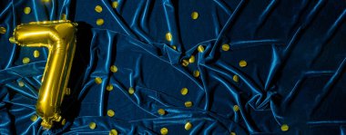 Mavi kadife üzerine yedi numaralı altın folyo balonu. Doğum günü tebrik kartında 7 yazılıydı. Altın sayılar ve kumaş arka plan. Işıltılı sayısal rakam. Pankart. Boşluğu kopyala