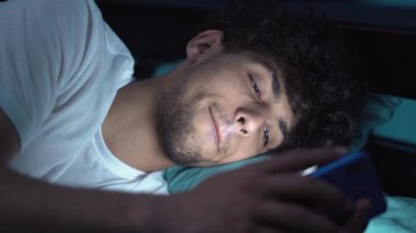 Gezici bağımlılık kavramı. Geceleri uykusuzluktan muzdarip, yataktaki akıllı telefonu kullanan Arap adam. Yakın plan.