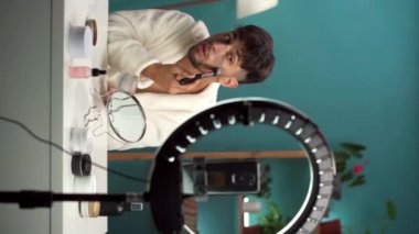 Erkek güzellik blogcusu bir blog için video kaydediyor, yüzüne maske takıyor, sosyal ağlardaki abonelerin cilt bakımından bahsediyor. Dikey video