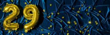 29 numara, altın folyo balon numarası mavi kadife arka planda, konfetiyle birlikte. Doğum günü tebrik kartı, 29. yazı. Yıldönümü etkinliği. Pankart. Şık altın rakamlı, parlak parlak bir ışık. Boşluğu kopyala,
