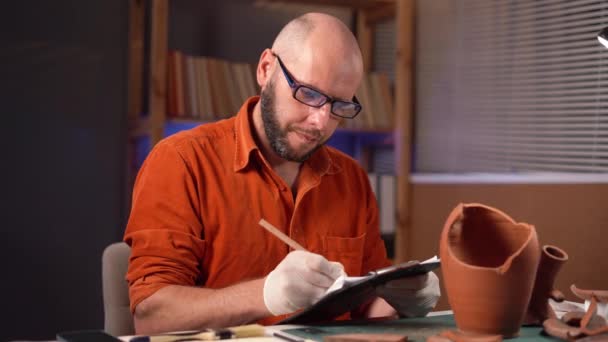 留胡子的男性考古学家在办公室工作到深夜 一边在写字板上写数据 一边坐着加班 复制空间 — 图库视频影像