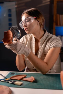 Geceleri en sevdiği hobisi ve arkeoloji bilimi doğrultusunda ofisinde çalışan antik bir amforanın parçalarını inceleyen bir arkeolog. Boşluğu kopyala