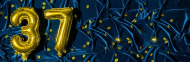 37 numara, altın folyo balon numarası mavi kadife arka planda, konfetiyle birlikte. Doğum günü tebrik kartı, 37. yazı. Yıldönümü etkinliği. Pankart. Şık altın rakamlı, parlak parlak bir ışık. Boşluğu kopyala,