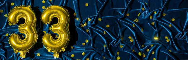 number thirty three, gold foil balloon number on blue velvet background with confetti. Birthday greeting card, inscription 33. Anniversary event. Banner. Stylish gold numeral, bright shiny shine. copy space,