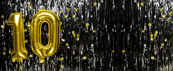 Gold foil balloon number number 10 on a background of black tinsel decoration. Birthday greeting card, inscription ten. Anniversary event. Banner. copy space.