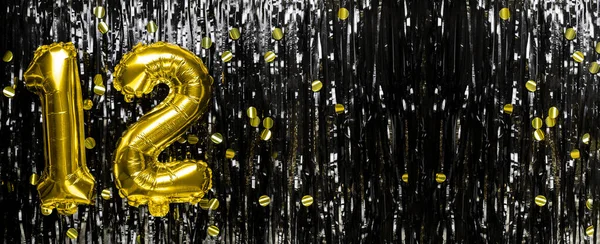 Gold foil balloon number number 12 on a background of black tinsel decoration. Birthday greeting card, inscription twelve. Anniversary event. Banner. copy space.