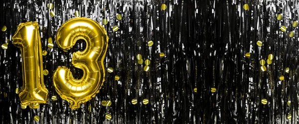 Gold foil balloon number number 13 on a background of black tinsel decoration. Birthday greeting card, inscription thirteen. Anniversary event. Banner. copy space.