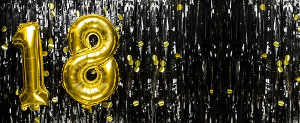 Gold foil balloon number number 18 on a background of black tinsel decoration. Birthday greeting card, inscription eighteen. Anniversary event. Banner. copy space.