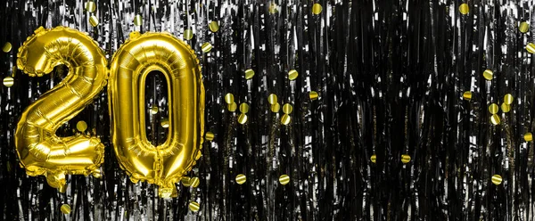 Gold foil balloon number number 20 on a background of black tinsel decoration. Birthday greeting card, inscription twenty. Anniversary event. Banner. copy space.