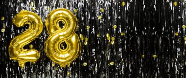 Siyah süslemenin arka planında 28 numaralı altın folyo balonu. Doğum günü tebrik kartı, yazıt 28. Yıldönümü etkinliği. Pankart. Boşluğu kopyala.