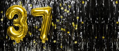 Siyah süslemenin arka planında 37 numaralı altın folyo balonu. Doğum günü tebrik kartı, 37 nolu yazı. Yıldönümü etkinliği. Pankart. Boşluğu kopyala.