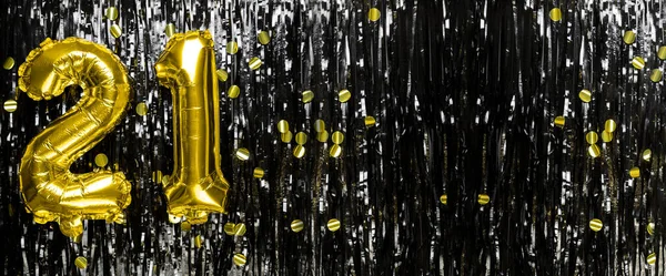 Gold foil balloon number number 21 on a background of black tinsel decoration. Birthday greeting card, inscription twenty one. Anniversary event. Banner. copy space.