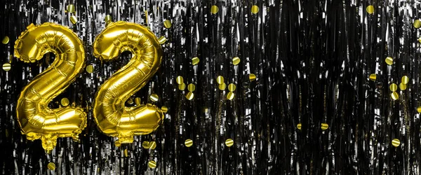 Gold foil balloon number number 22 on a background of black tinsel decoration. Birthday greeting card, inscription twenty two. Anniversary event. Banner. copy space.