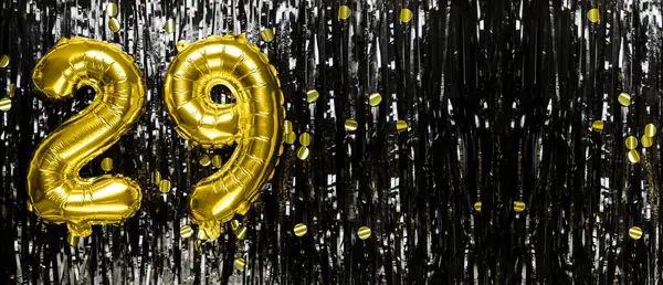 Gold foil balloon number number 29 on a background of black tinsel decoration. Birthday greeting card, inscription twenty nine. Anniversary event. Banner. copy space.