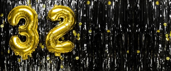 Gold foil balloon number number 32 on a background of black tinsel decoration. Birthday greeting card, inscription thirty two. Anniversary event. Banner. copy space.