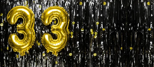 Gold foil balloon number number 33 on a background of black tinsel decoration. Birthday greeting card, inscription thirty three. Anniversary event. Banner. copy space.