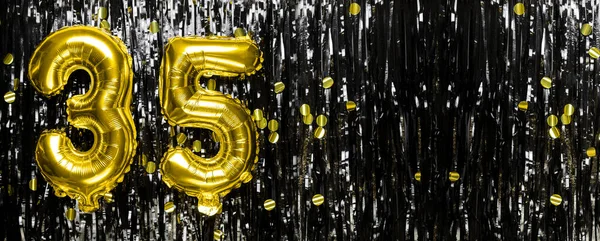 Gold foil balloon number number 35 on a background of black tinsel decoration. Birthday greeting card, inscription thirty five. Anniversary event. Banner. copy space.