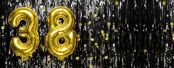 Gold foil balloon number number 38 on a background of black tinsel decoration. Birthday greeting card, inscription thirty eight. Anniversary event. Banner. copy space.