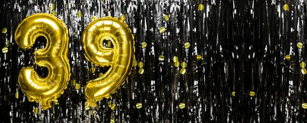 Gold foil balloon number number 39 on a background of black tinsel decoration. Birthday greeting card, inscription thirty nine. Anniversary event. Banner. copy space.