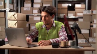 Dizüstü bilgisayarı olan depo genç erkek yöneticisi veri tabanına envanter bilgilerini giriyor. Boşluğu kopyala