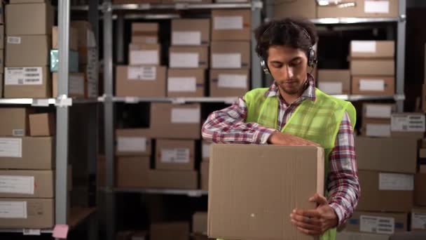 阿拉伯男子头戴无线耳机 在配送仓库里工作 手里拿着定单 装着盒子 看着相机 面带微笑 复制空间 — 图库视频影像
