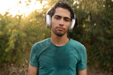 Yaz yağmurunda ıslanan kulaklıklı üzgün genç adam. Adam yağmurda yürüyor. Boşluğu kopyala