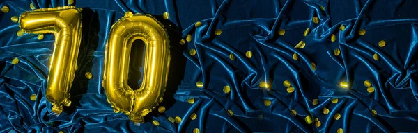 Gold foil balloon number number 70 on a background of blue velvet decoration. Birthday greeting card, inscription seventy. Anniversary event. Banner. Copy space