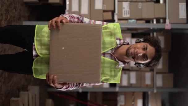 阿拉伯男子头戴无线耳机 在配送仓库里工作 手里拿着定单 装着盒子 看着相机 面带微笑 复制空间 复制空间 — 图库视频影像
