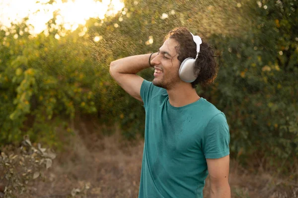 Young man dancing in the forest and listening music in headphones. Guy enjoying a summer rain. Copy space