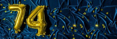 Mavi kadife dekorasyonun arka planında 74 numaralı altın folyo balonu. Doğum günü tebrik kartı, 74 'üncü yazı. Yıldönümü etkinliği. Pankart. Boşluğu kopyala