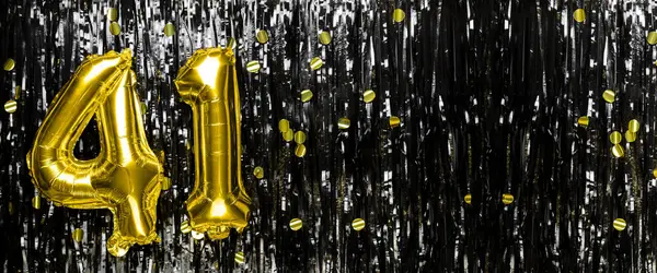 Gold foil balloon number number 41 on a background of black tinsel decoration. Birthday card, inscription forty-one. Anniversary event. Banner. copy space.
