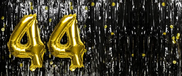 Gold foil balloon number number 44 on a background of black tinsel decoration. Birthday card, inscription forty-four. Anniversary event. Banner. copy space.
