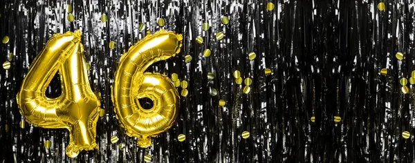 Gold foil balloon number number 46 on a background of black tinsel decoration. Birthday card, inscription forty-six. Anniversary event. Banner. copy space.