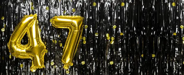 Gold foil balloon number number 47 on a background of black tinsel decoration. Birthday card, inscription forty-seven. Anniversary event. Banner. copy space.
