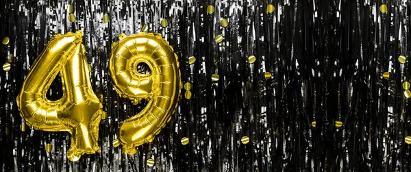 Gold foil balloon number number 49 on a background of black tinsel decoration. Birthday card, inscription forty-nine. Anniversary event. Banner. copy space.