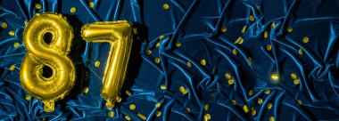 87 numaralı altın folyo balonu. Üzerinde 87 yazan doğum günü ya da yıldönümü kartı. Mavi kadife arka plan. Yıldönümü kutlaması. Pankart. Boşluğu kopyala