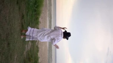 Yazlık elbiseli şehvetli bir kadın akşamları sahilde yürüyor. Genç bayan cennet kumsalında dinleniyor. Dikey video