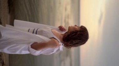 Yazlık elbiseli şehvetli bir kadın akşamları sahilde yürüyor. Genç bayan cennet kumsalında dinleniyor. Dikey video