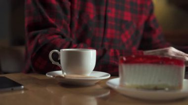Resmi giysiler içinde isimsiz bir erkek, kafede kahveye şeker koyarken cheesecake ile masada oturuyor. Yakın plan.