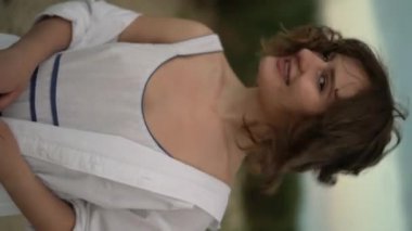 Mutlu gülümseyen, gevşek saçlı, doğada özgürlüğün tadını çıkaran genç kadın kameraya bakıyor, yakından. Dikey video