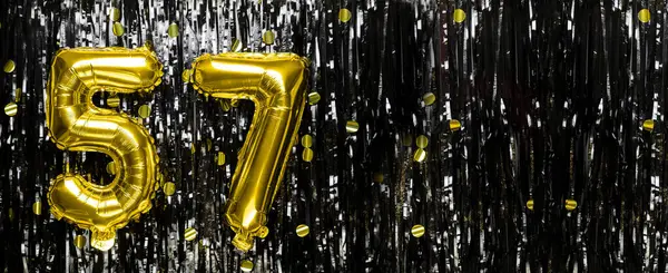 Gold foil balloon number number 57 on a background of black tinsel decoration. Birthday card, inscription fifty-seven. Anniversary event. Banner. copy space.