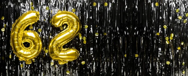 Gold foil balloon number number 62 on a background of black tinsel decoration. Birthday greeting card, inscription sixty-two. Anniversary event. Banner. copy space.